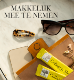 Twee Collagen Shot™ sticks liggen in een geopende tas naast een zonnebril, telefoon en accessoires, met de tekst Makkelijk mee te nemen.