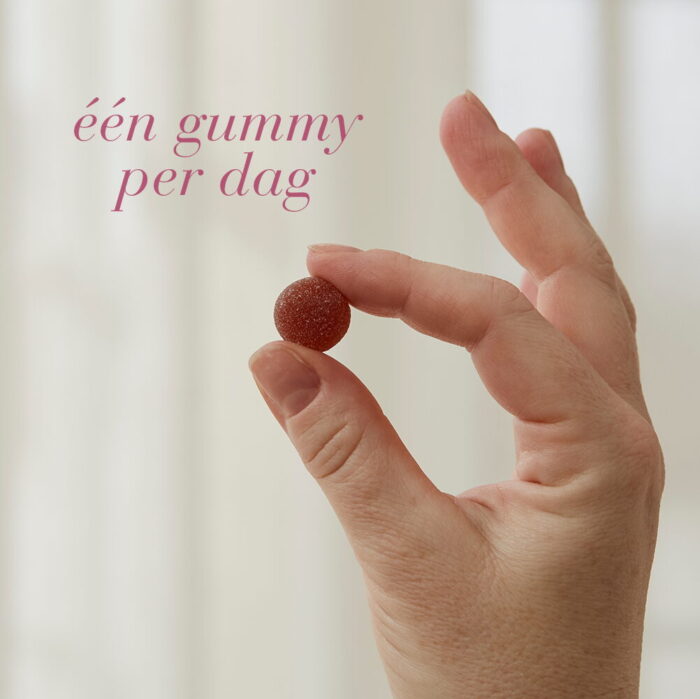 Hand houdt één gummy vast met de tekst "één gummy per dag".