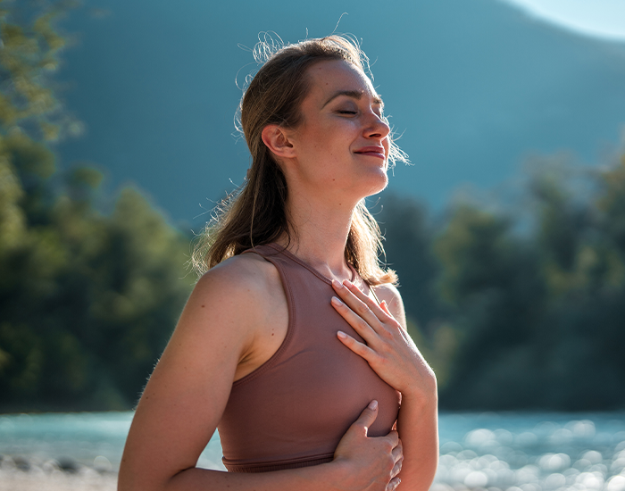 Vrouw houdt haar borst vast en glimlacht in de natuur.