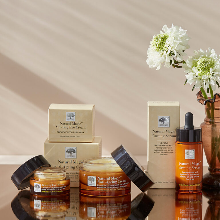 Natural Magic™ verpakkingen en crèmepotten met daarnaast een vaas met witte bloemen.