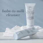 Verpakking van Deep Cleanse™ Black Bee Honey Cleansing Balm op een handdoek met de vermelding Balm-to-milk cleanser.