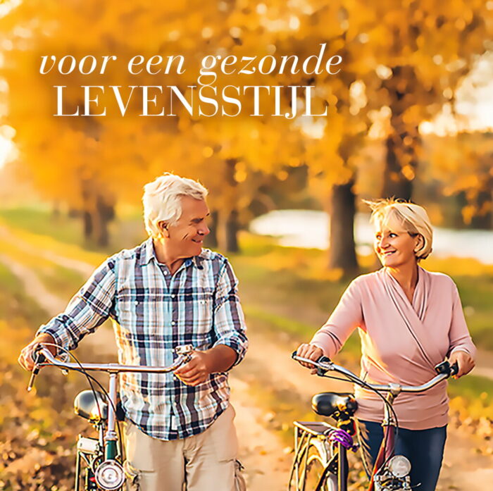 Ouder koppel wandelt met fietsen door een park in herfstkleuren, als illustratie van een gezonde en actieve levensstijl.