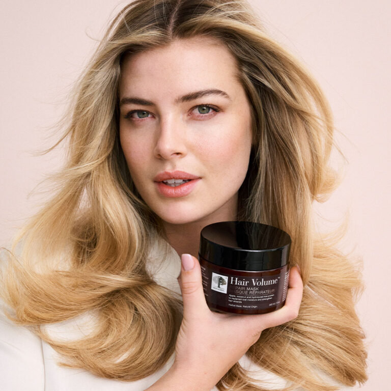 Vrouw met volumineus blond haar houdt Hair Volume™ Repair Mask vast.