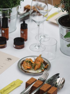 De helende kracht van de natuur – New Nordic-persevenement in Restaurant De kas 11 Gedekte tafel met gerecht, Natural Magic™ producten en een Collagen Shot™ sachet tijdens een New Nordic kruiden evenement.